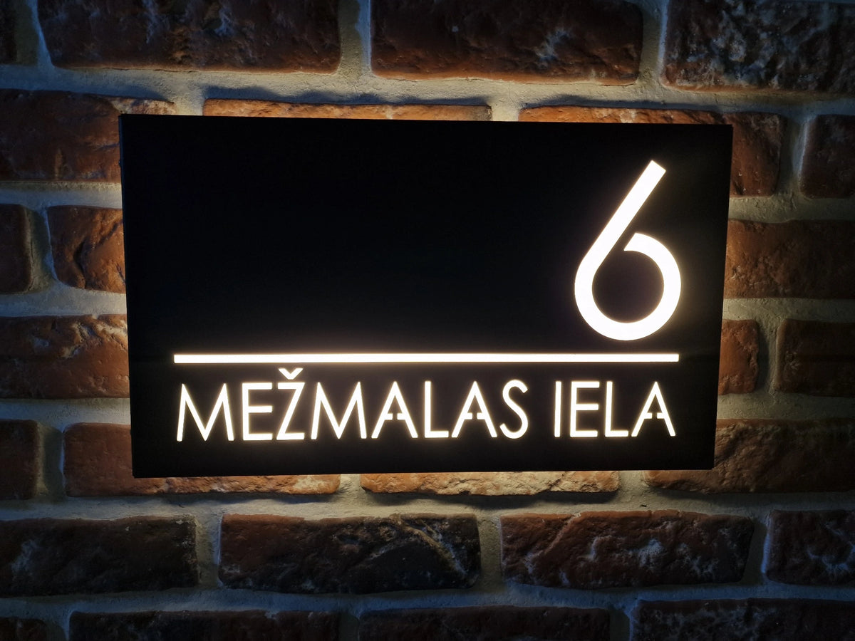 Black horizontal LumiSign Horizon with illuminated number 6 and MEŽMALAS IELA lettering on a brick wall.