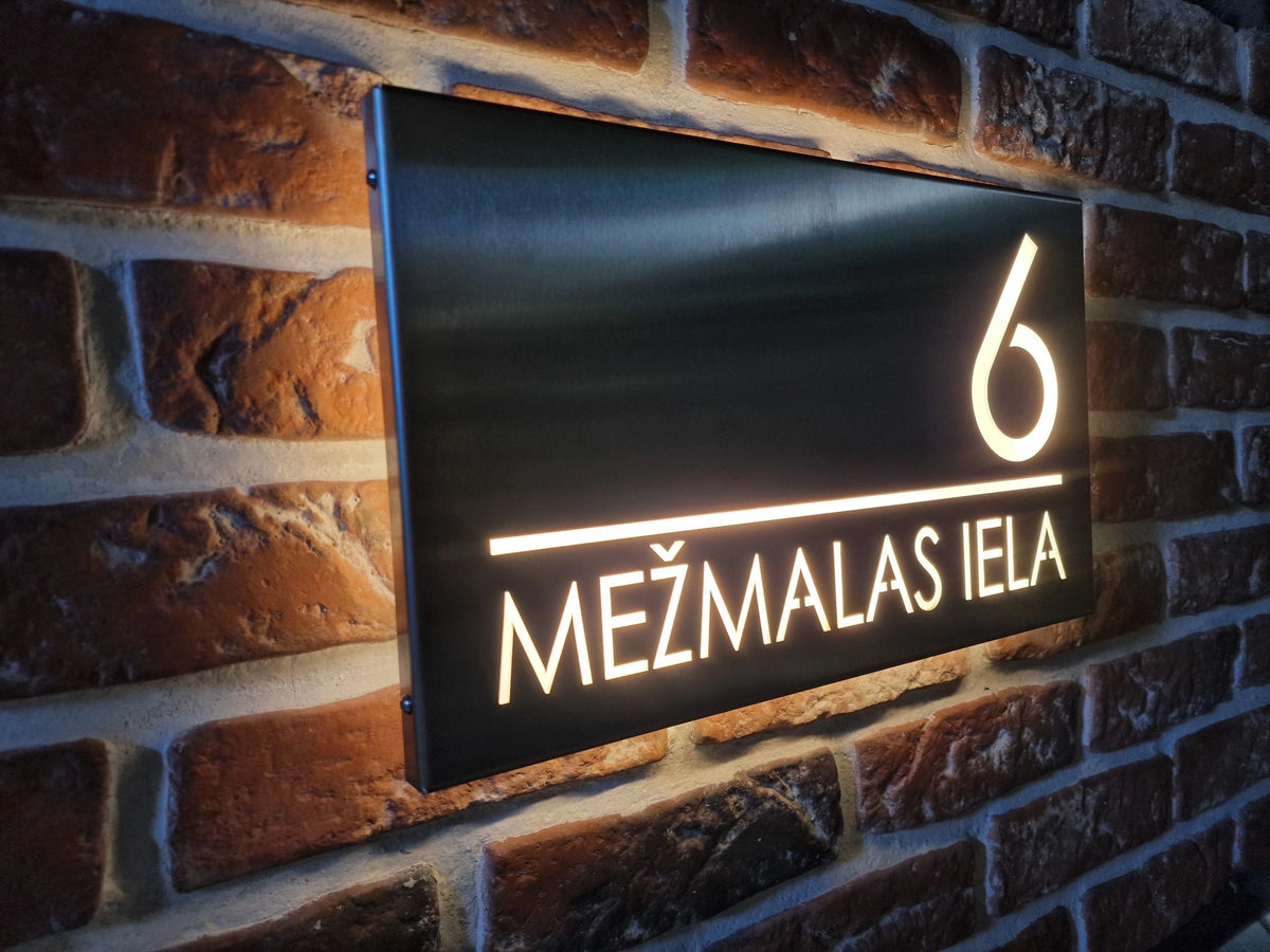 Angled view of a stainless-steel horizontal LumiSign Horizon on brick, with glowing number 6 and MEŽMALAS IELA lettering.